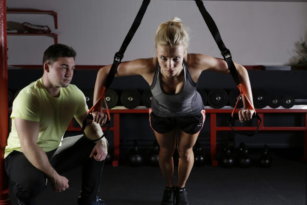 Top 3 Fitness Brands for Wholesale, A woman performing strength training with a trainer in a gym setting, showcasing fitness and dedication.